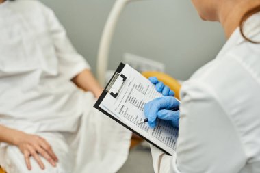 Bir jinekolog, klinikte sağlık değerlendirmesi yaparken hasta bilgilerini inceler..
