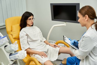 Laboratuvar önlüklü bir jinekolog klinikte bir kadın hastayla sağlık sorunlarını tartışıyor..