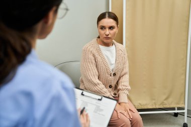 Laboratuvar önlüklü bir jinekolog klinikte bir kadın hastayla sağlık sorunlarını tartışıyor..