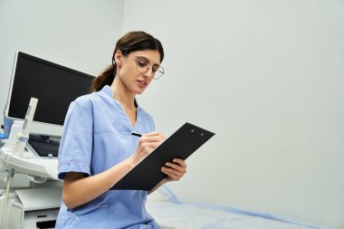 Laboratuvar önlüklü bir jinekolog, klinikte tedavi görürken hasta bilgilerini kaydeder..