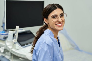 Laboratuvar önlüğü giymiş yetenekli bir jinekolog klinikte kadın sağlığıyla ilgilenirken sıcak bir şekilde gülümser..