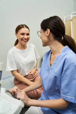 Bir jinekolog, klinikte sağlık kontrolü sırasında gülümseyen bir hastayla meşgul oluyor..
