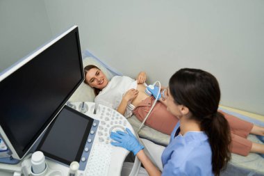 Bir jinekolog modern bir klinikte rahat bir kadına detaylı bir ultrason uygular..