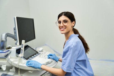 Laboratuvar önlüklü kendini adamış bir jinekolog ultrason cihazı kullanırken gülümsüyor..