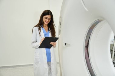 Laboratuvar önlüklü profesyonel doktor ileri MR cihazlarının yakınındaki hasta teşhislerini inceliyor..