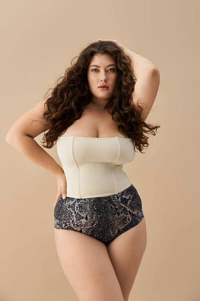 Уверенная молодая женщина демонстрирует свою красоту в модном нижнем белье на мягком фоне.