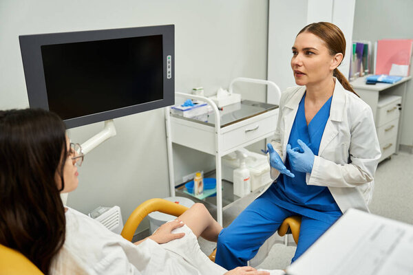 A gynecologist discusses health concerns with a female patient in a well-equipped clinic.