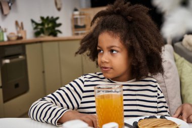 Little girl enjoys a cozy breakfast at home. clipart