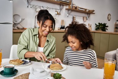 A mother and her daughter enjoy a joyful breakfast filled with pancakes and berries at home. clipart