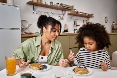 Mother and daughter enjoy a delightful breakfast together, savoring pancakes topped with berries. clipart