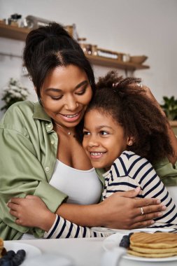 Bir anne, sevgi ve kahkahayla dolu kahvaltısını yaparken neşeli kızını kucaklar..