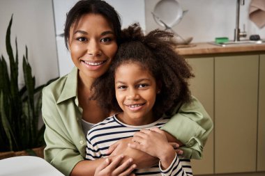 A mother and her little girl share joyful moments while embracing each other at home. clipart