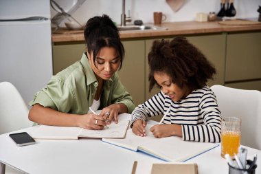 Mother and daughter are happily engaged in creative activities at their kitchen table. clipart