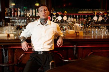 Dövmeli genç bir adam, gece hayatı atmosferinde yaşarken barda rahatlar..