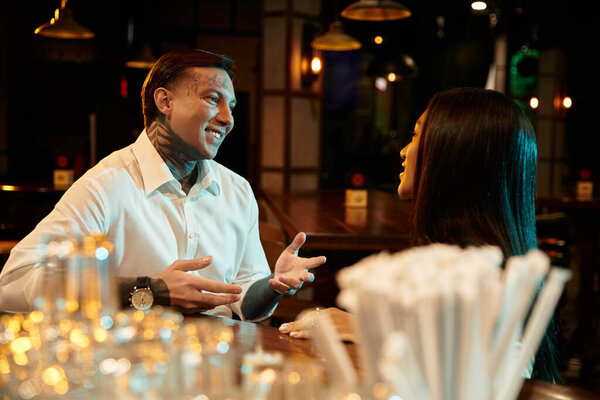 Tattooed young couple shares laughter and connection over drinks during a lively night out.