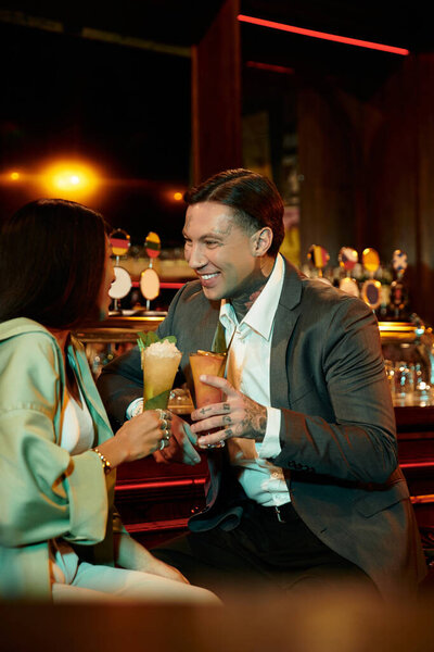 Young couple celebrating their connection over vibrant cocktails in an upscale bar setting.