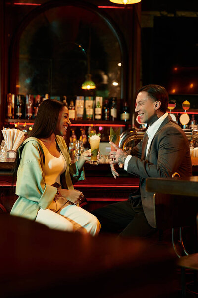 A young couple shares laughter and drinks at a lively bar, enjoying their night out.