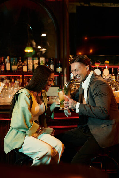 Tattooed couple shares laughter and drinks on a cozy date in a trendy bar setting.