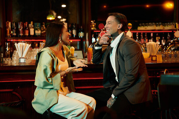 Young couple shares laughter and connection over drinks during a night out at a bustling bar.