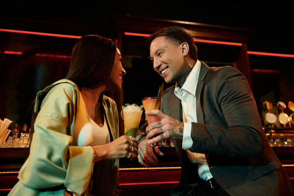 A tattooed man and woman share laughter and cocktails during a lively evening together.