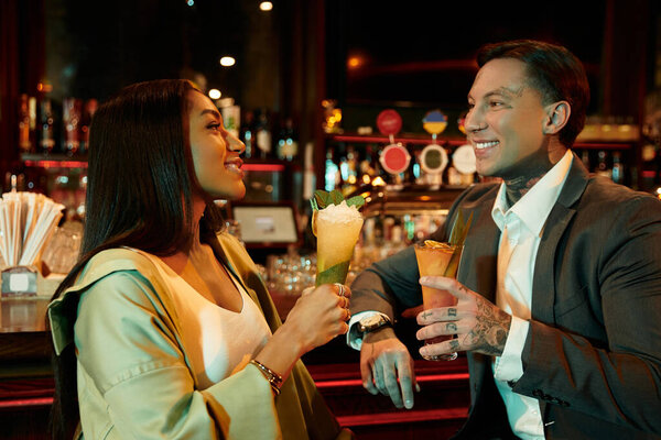 Tattooed couple sharing drinks and laughter on a cozy evening at a vibrant bar.