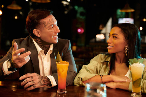 A young multicultural couple shares laughter and cocktails during a lively evening at the bar.