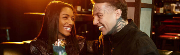 Мультикультурная пара смеется в течение оживленного вечера в баре, наслаждаясь свиданием.