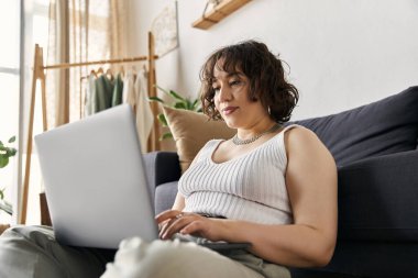 Young woman with curly hair relaxes while working on her laptop in a beautifully designed apartment. clipart