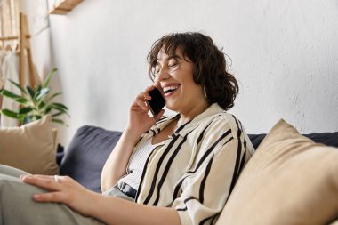 Cheerful young woman with curly hair connects with a friend in her trendy, sunlit living space. clipart