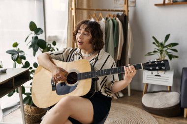 Kıvırcık saçlı güzel bir kadın modern dairesinde gitar çalıyor, neşe saçıyor..