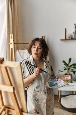Güzel kıvırcık saçlı genç bir kadın modern dairesinde tutkuyla sanat yaratıyor..