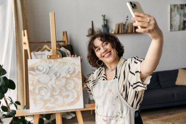Genç ressam, parlak ve şık bir dairede tuvalinin yanında neşeyle selfie çekiyor..