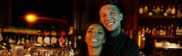 Tattooed couple enjoys a joyful night out in a lively bar atmosphere.