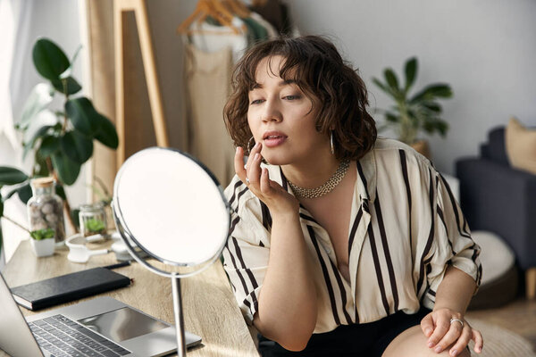 A young woman applies lipstick in a sunlit apartment, gazing at herself in the mirror.