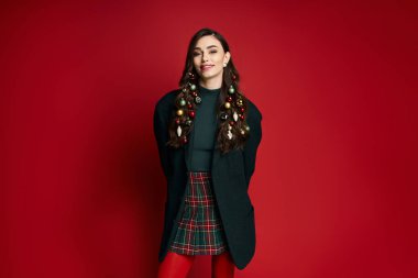 Confident young woman dons festive hair decor against a striking red backdrop. clipart