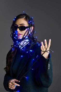 Mavi ışıklara sarılı güzel genç bir kadın stüdyo ortamında eşsiz bir moda gösterisi sergiliyor..