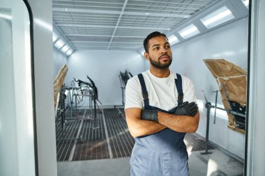 Eldiven giyen yakışıklı tamirci, parlak bir oto atölyesine özgüvenle poz veriyor..