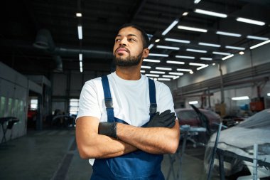 Handsome mechanic stands proudly in a well lit garage, showcasing his skills and dedication. clipart