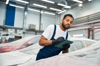 Skilled mechanic inspects vehicles while taking notes in a modern automotive workshop clipart