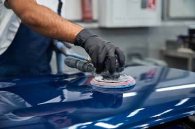 A young, handsome mechanic meticulously works on polishing a cars surface in a bright workshop. clipart