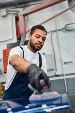 Genç adam modern bir otomotiv atölyesinde bir araç yüzeyini cilalamaya odaklanmış..