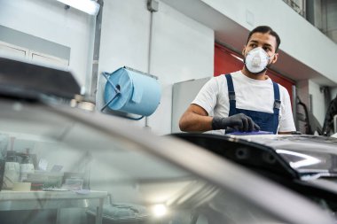 Bir atölyede maske ve eldiven giyerken tulumlu genç tamirci görevine odaklanıyor.