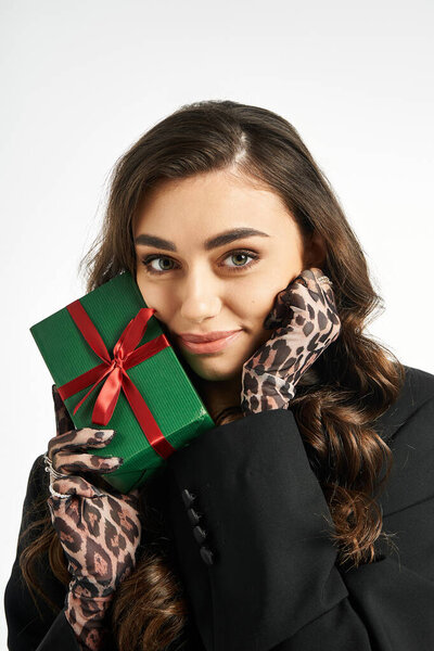 A beautiful young woman smiles while holding a green gift adorned with a red ribbon.