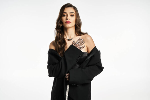 Young woman poses confidently in a black oversized coat, highlighting her stylish hand tattoos.