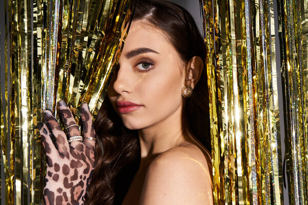 Captivating young woman showcases her charm with stylish attire near golden decorations