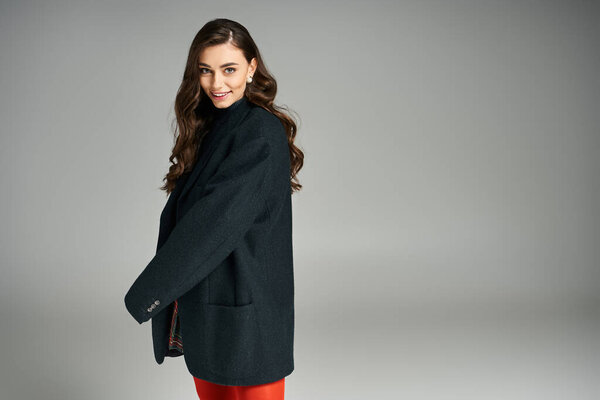 Confident young woman showcases vibrant outfit with a chic coat while smiling warmly.
