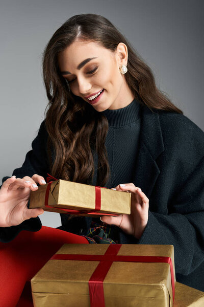 A young woman with a warm smile opens a golden wrapped present adorned with a red ribbon.