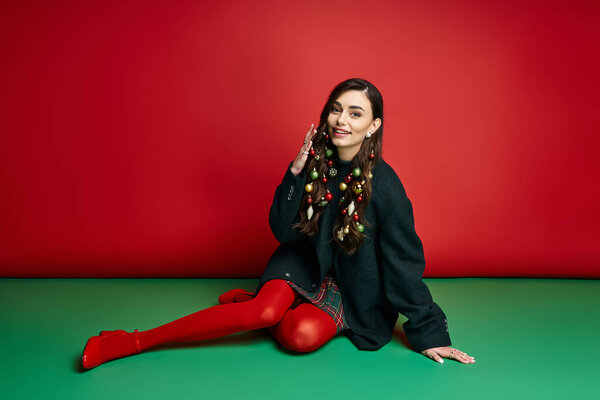 Ярко одетая женщина с радостью демонстрирует праздничный декор на веселом красном фоне.