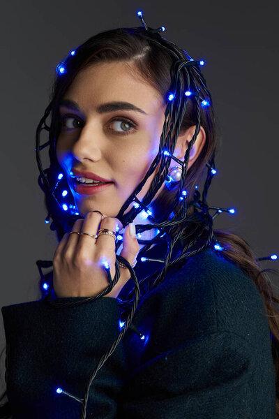 A pretty young woman playfully wraps herself in blue string lights, showcasing her creativity.