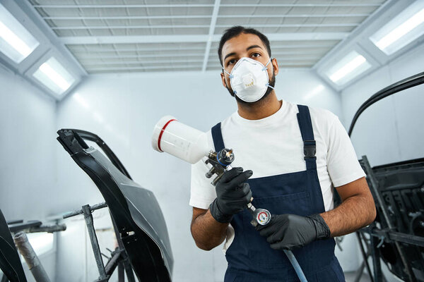 Молодой механик в маске готовится покрасить автомобиль в чистую мастерскую.